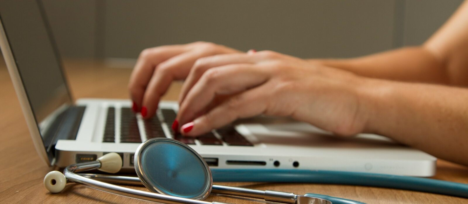 person sitting while using laptop computer and green stethoscope near