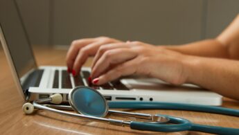 person sitting while using laptop computer and green stethoscope near